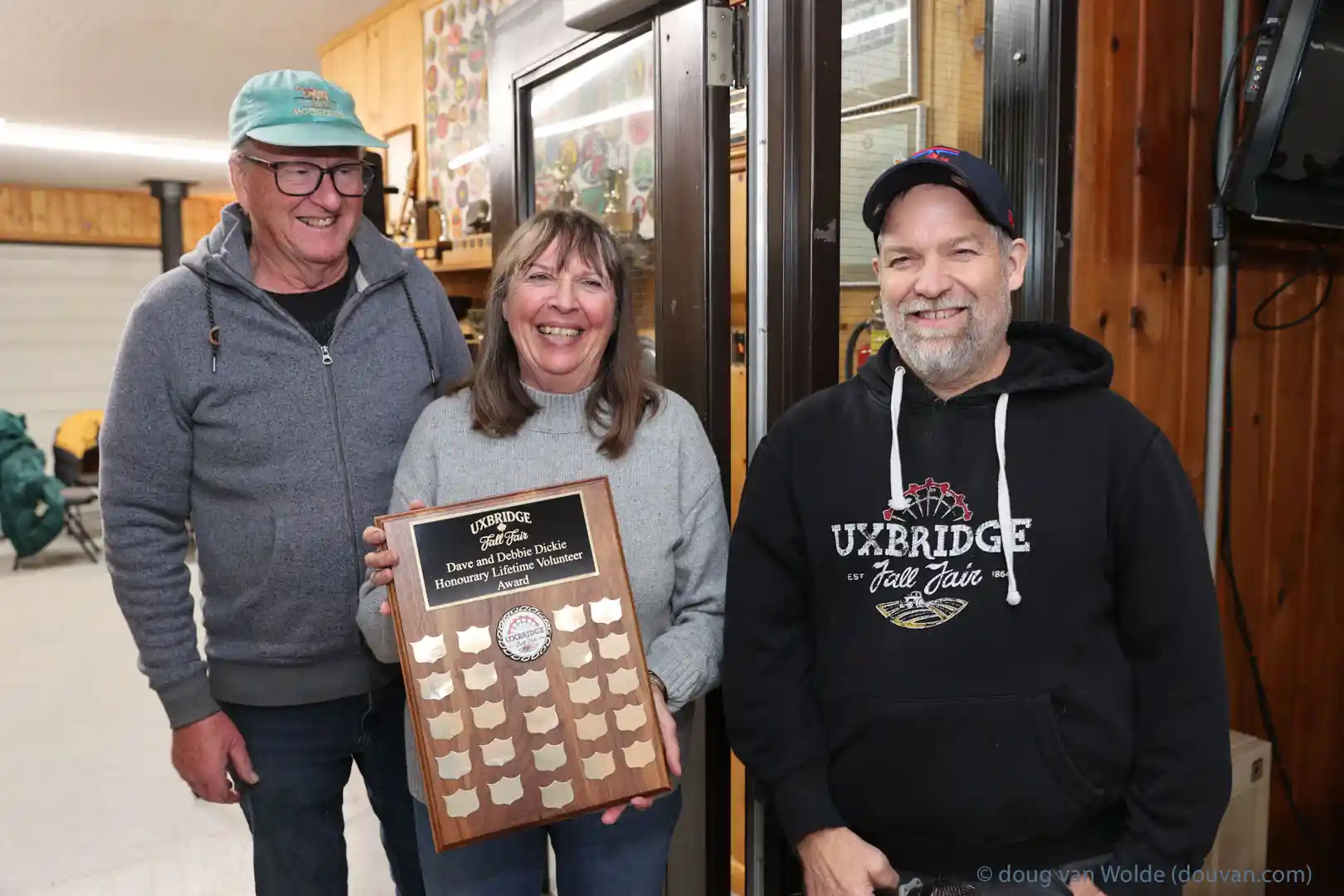 Dave Dickie, Debbie Dickie and Rob Ashton smiling as Debbie holds the new Honourary Lifetime Volunteer Award plaque